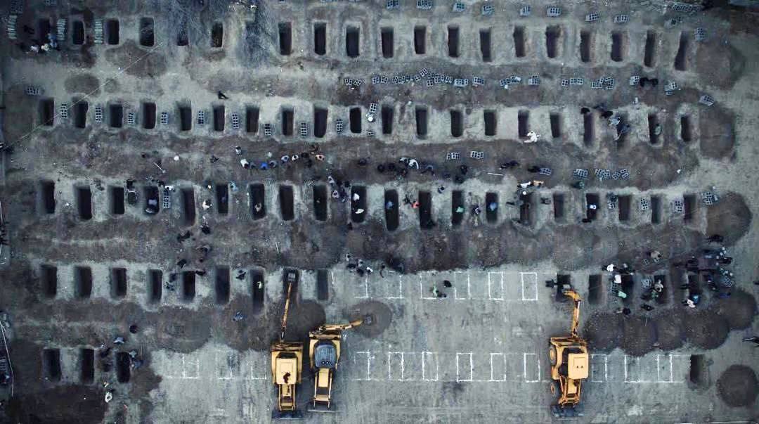 Drone overhead image of rows of small rectangular graves being excavated in a cemetery in Minab, Iran, with yellow excavators and workers present, for burying 165 child victims of the US-Israel joint attack on a school in March 2026