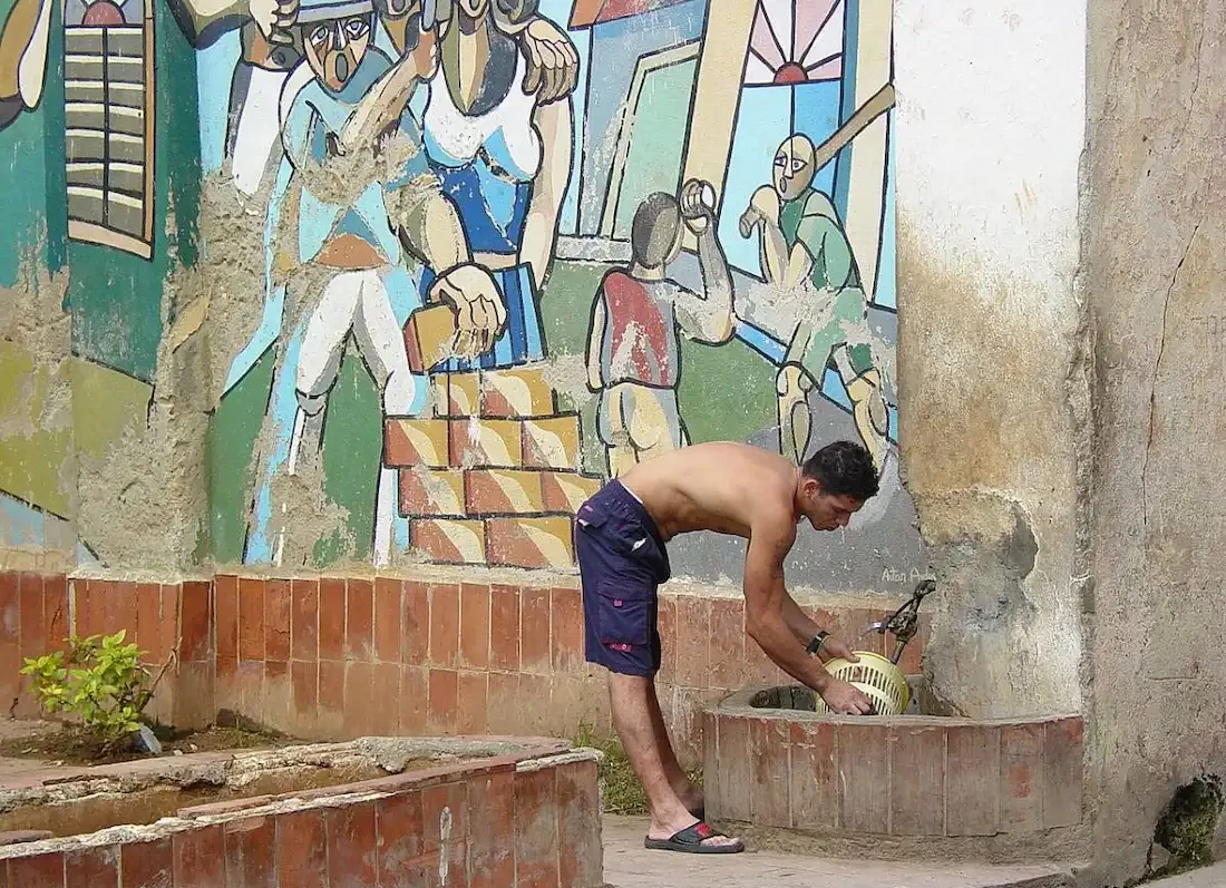 A man fills containers with water from a public tap on a street in Habana Vieja, Havana, Cuba.