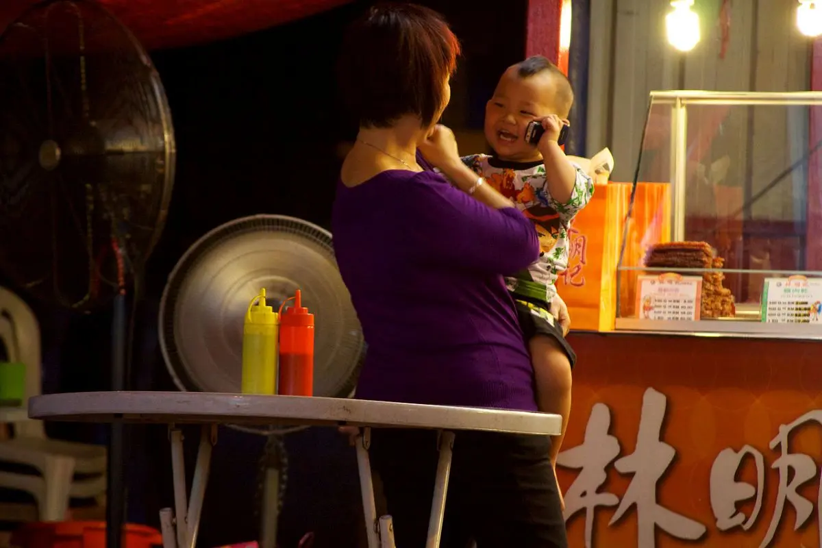 A mother and baby in Malaysia sharing a mobile phone — a scene highlighting the ubiquity of digital devices among all ages, now at the centre of new social media age bans and rising privacy concerns.