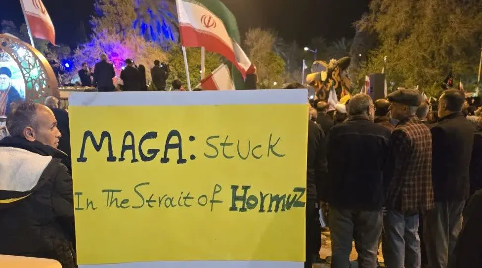 A placard reading "MAGA: stuck in the strait of Hormuz" at a pro-Iran demonstration referencing the "Make America Great Again" (MAGA) political slogan, which is challenged by the Iranian closure of the strategic Strait of Hormuz, a key chokepoint for oil exports.